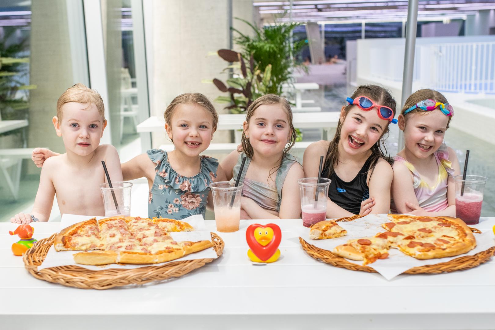 Kids enjoying pizzas around a table and smiling